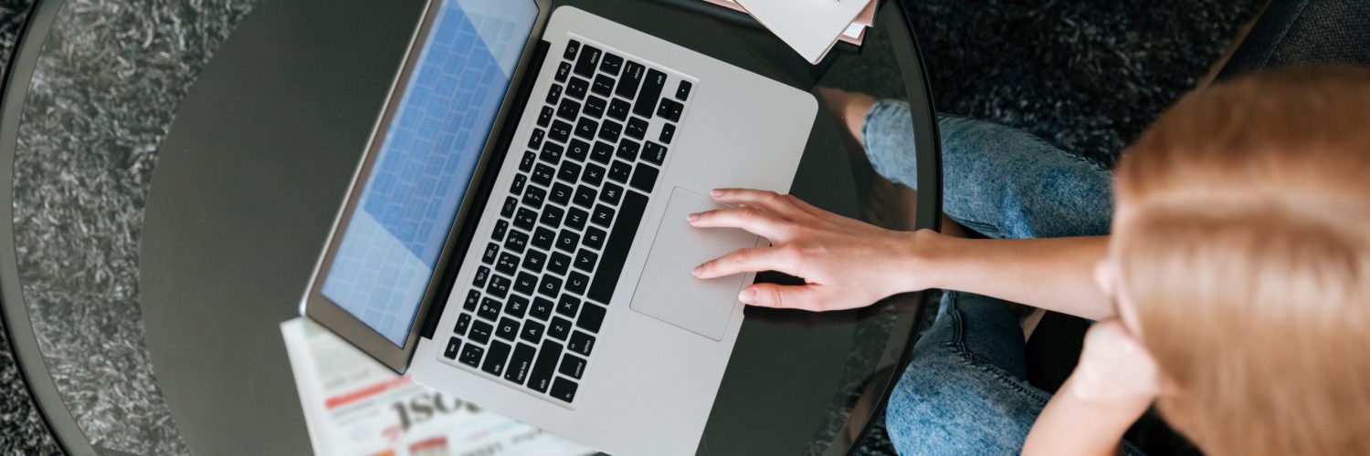 Top view of woman drinking tea and using laptop on glass table at home